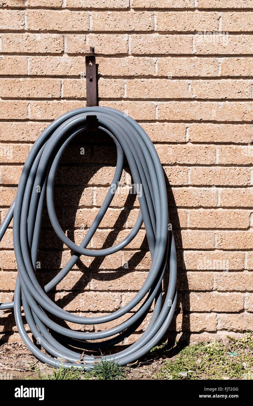 A rolled up water hole on a hanger hanging on the side of a brick home. Stock Photo