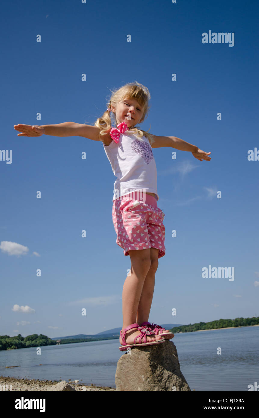 adorable happy girl standing in the rock by the blue river and blue sky ...