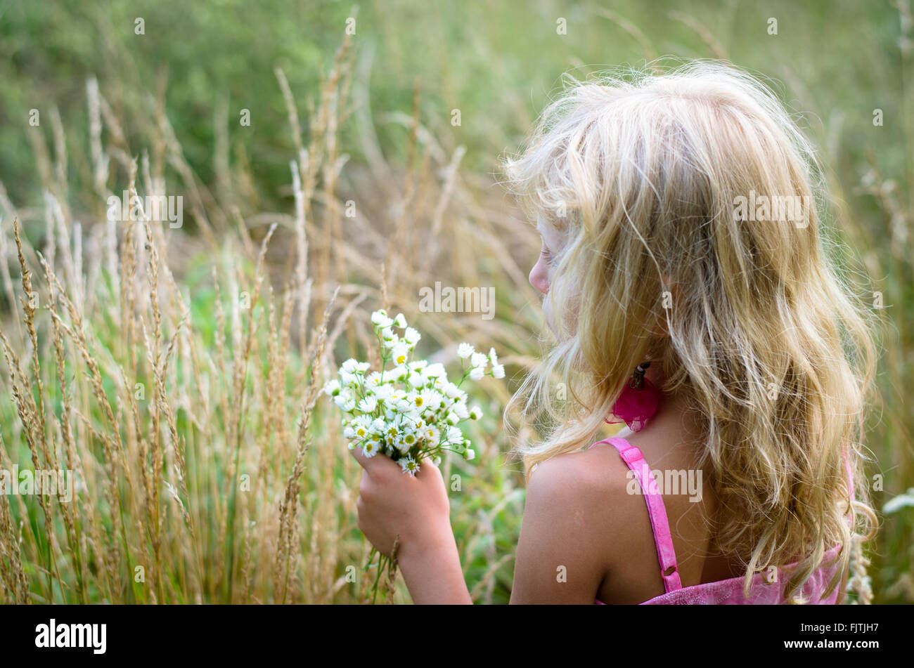 little girl with long blond hair and bunch of flowers in the meadow back view Stock Photo