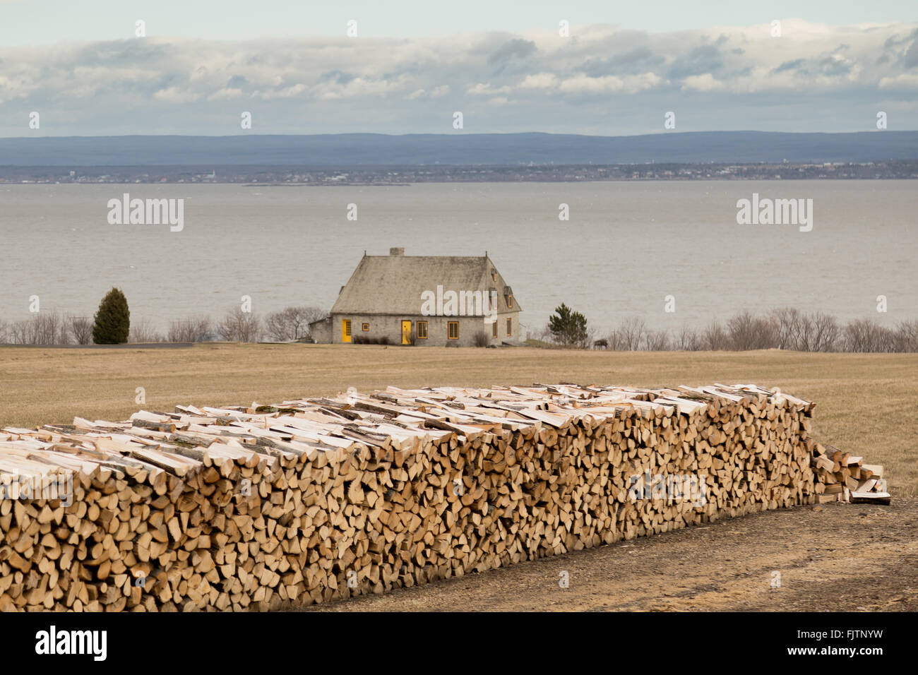 Long pile of cut firewood logs and stone house in a field on the St Lawrence River, Ile d'Orleans, Quebec, Canada. Stock Photo