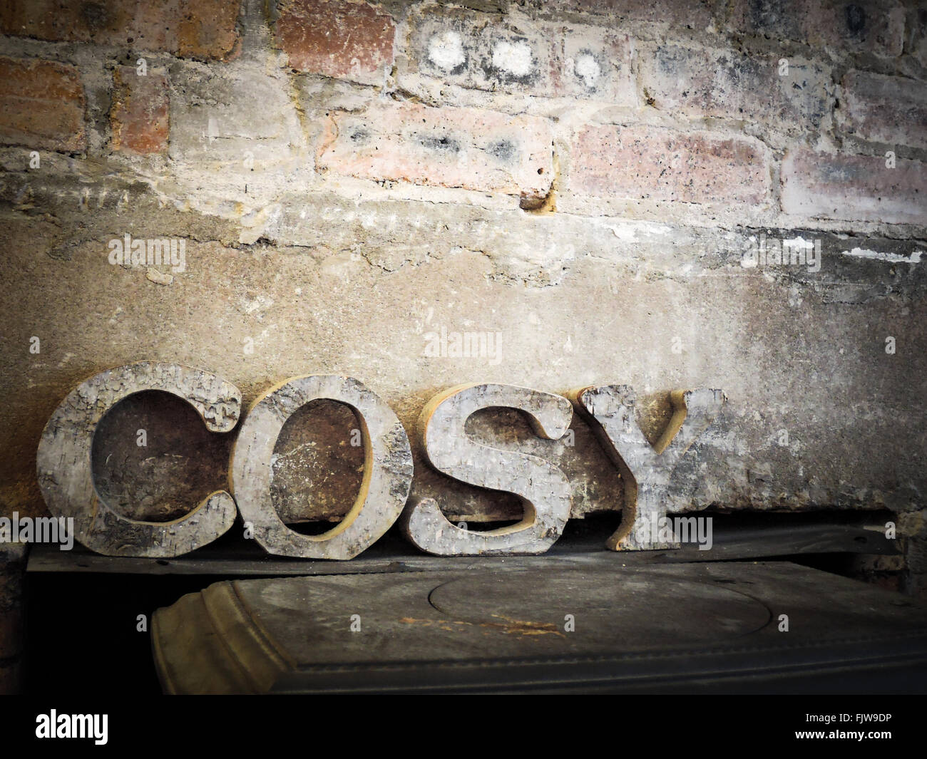 COSY decorating letters against a rustic brick wall above a wood burning stove Stock Photo