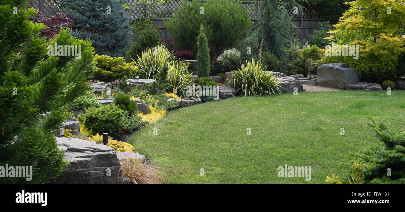Naturally sculptured flat top rocks from northwest Oregon are placed in a beautifully landscaped backyard with perennials. Stock Photo