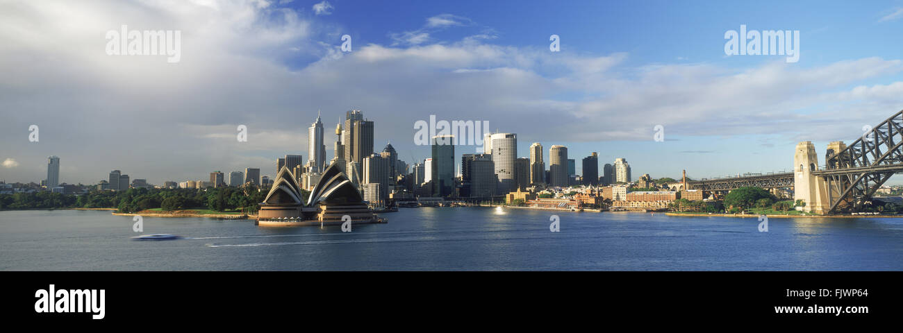 Panoramic view of Sydney skyline with Opera House and Harbour Bridge on right with ferryboat crossing Stock Photo