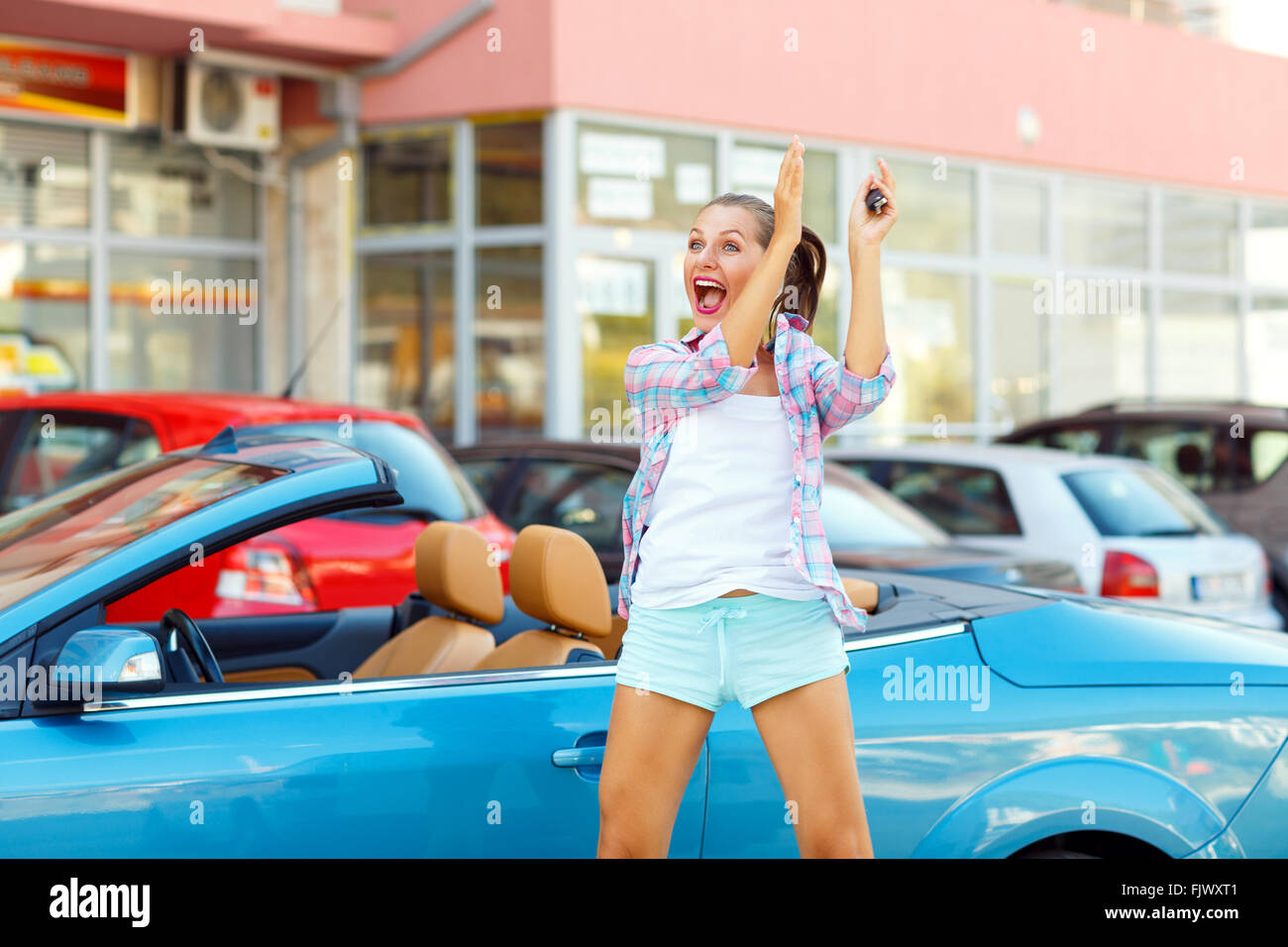 Young emotional woman standing near a convertible with the keys in her hand - concept of buying a used car or a rental car Stock Photo