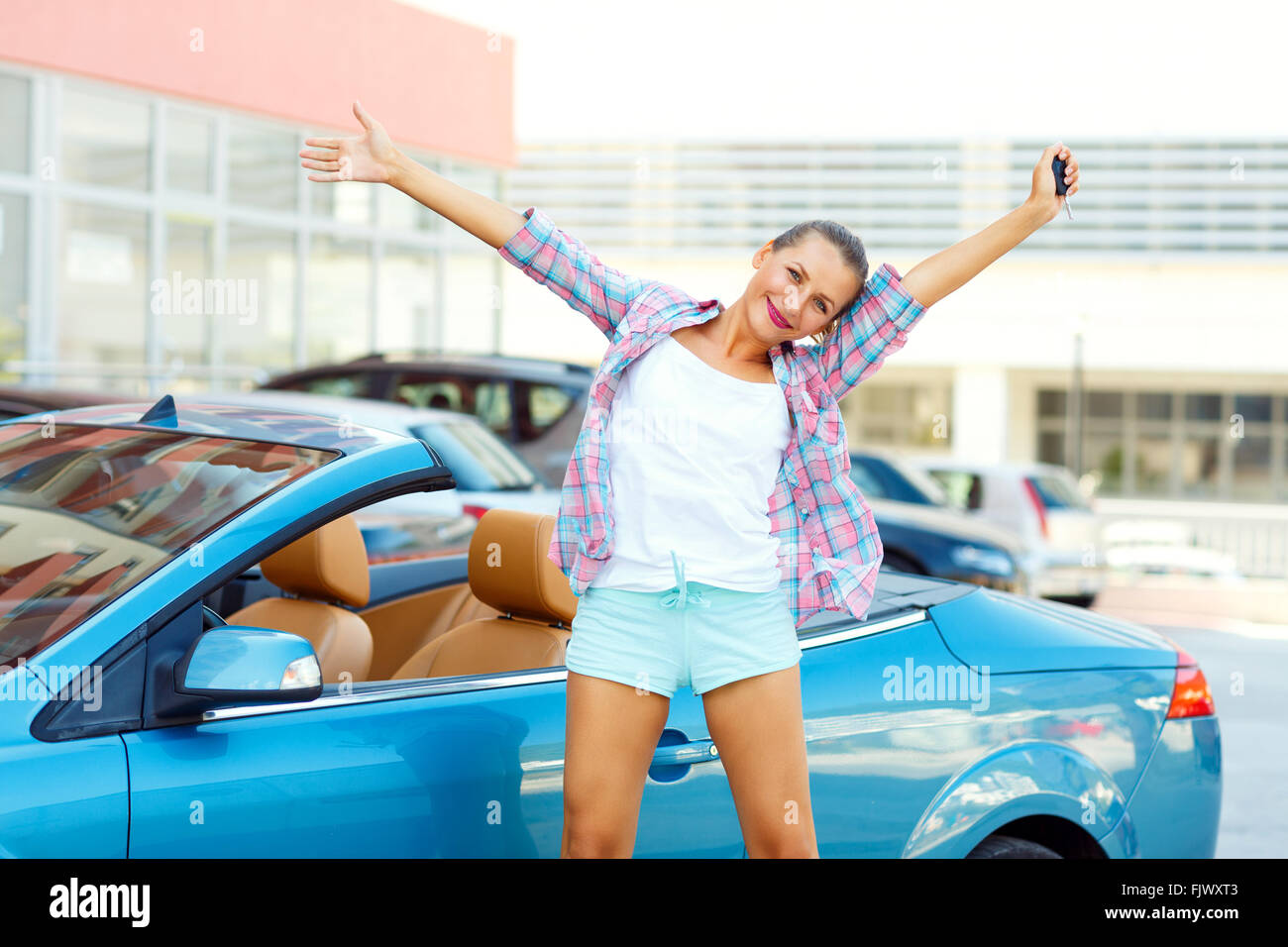 Young emotional woman standing near a convertible with the keys in her hand - concept of buying a used car or a rental car Stock Photo
