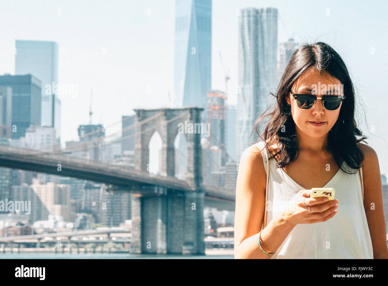 Young Woman Using Smart Phone Against Brooklyn Bridge Stock Photo
