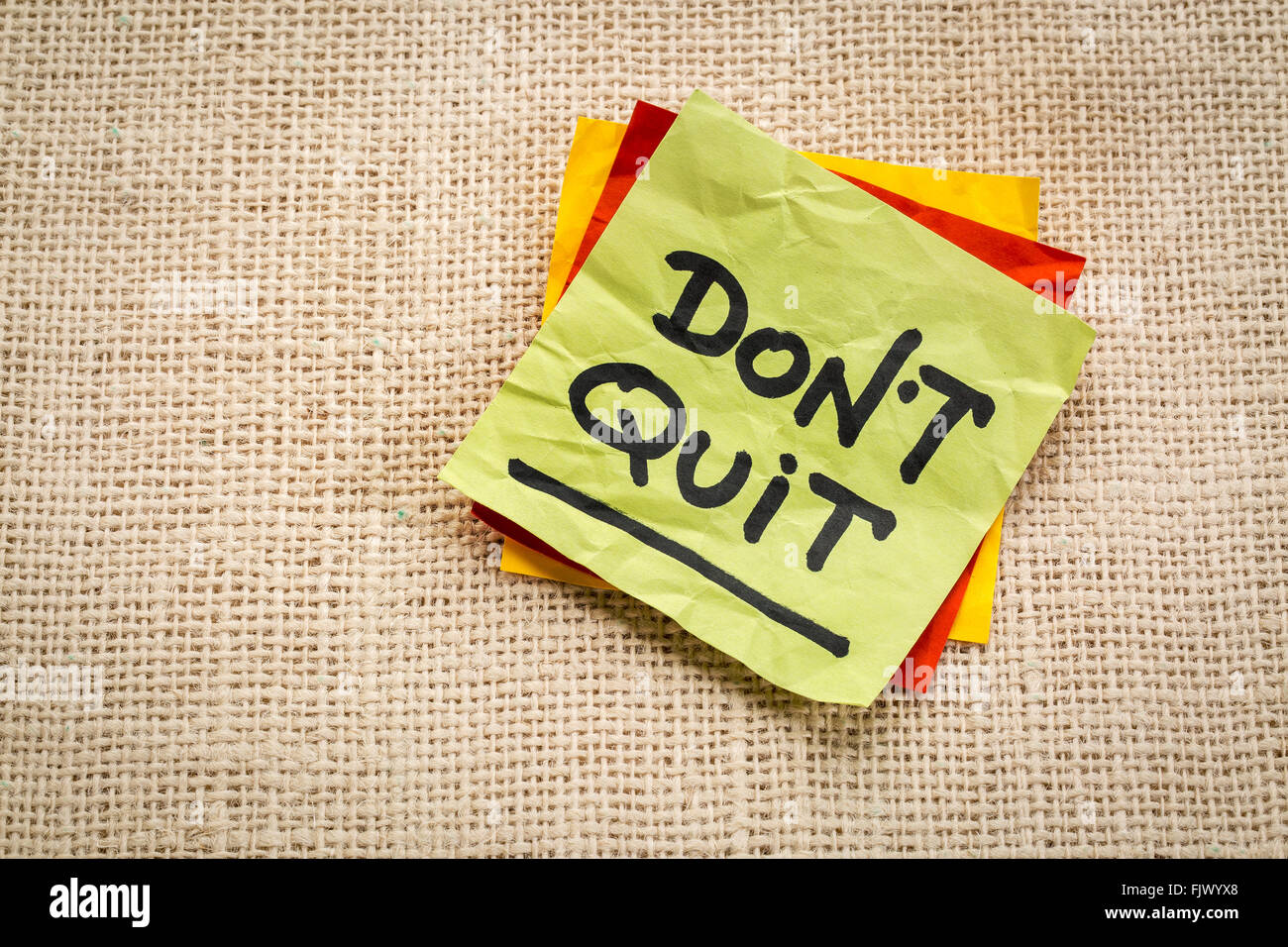 Do not quit advice or reminder on a  sticky note against burlap canvas Stock Photo