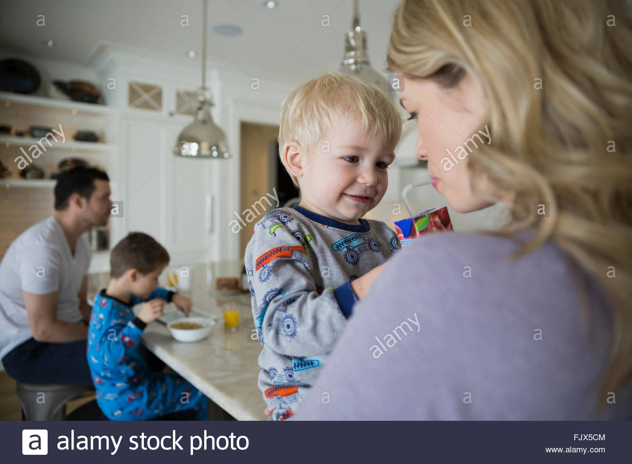 Son sharing juice box with mother in kitchen Stock Photo
