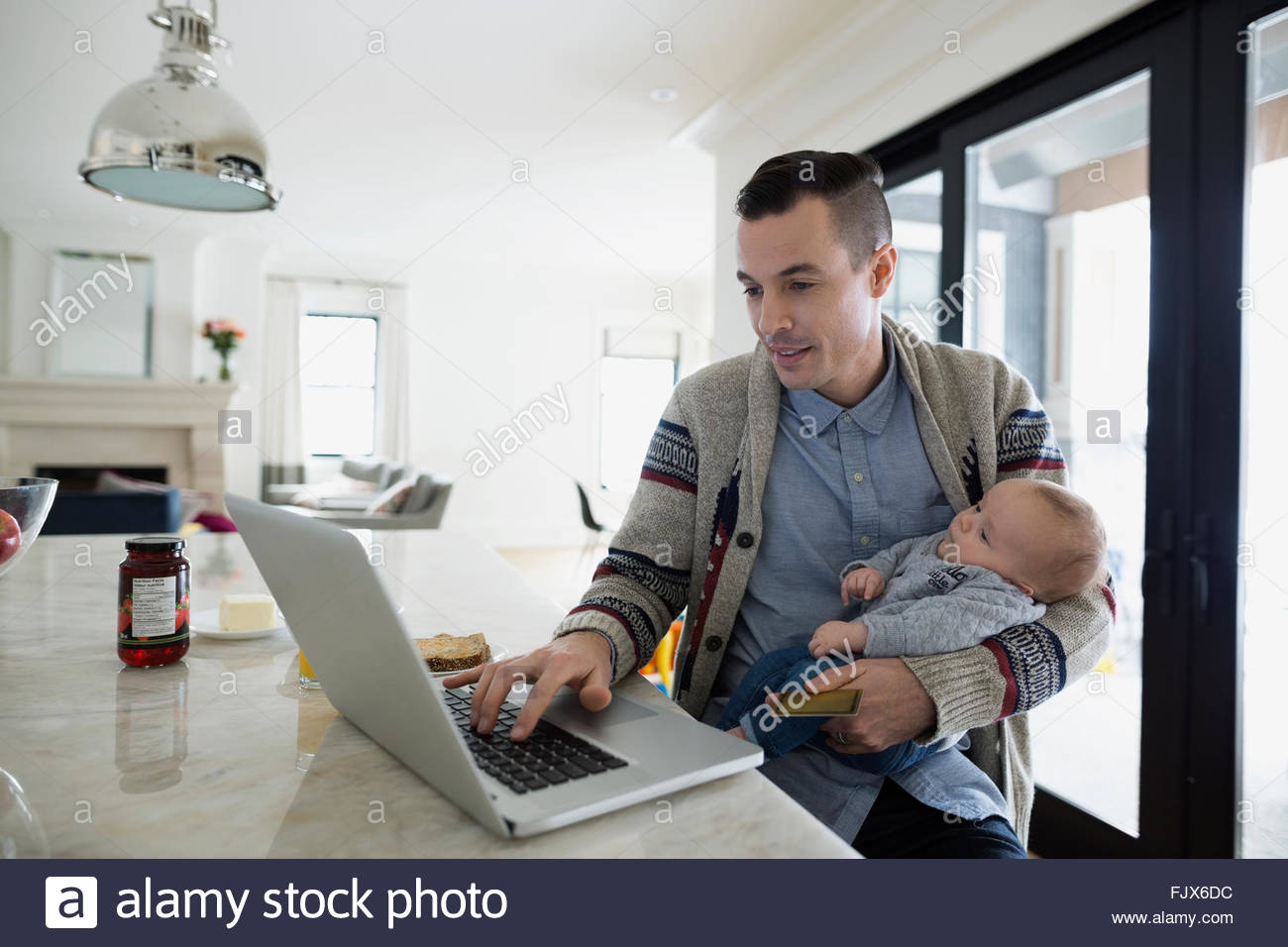 Father holding baby son and working at laptop Stock Photo