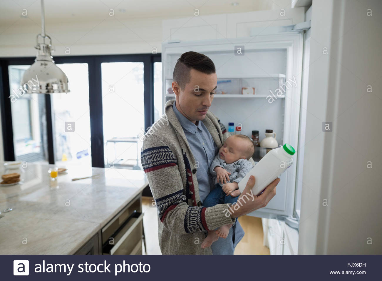 Father holding baby son checking milk at refrigerator Stock Photo