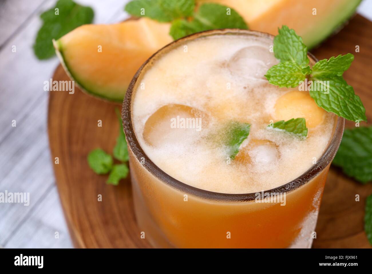 Fresh cantaloupe melon juice with ice cubes; garnished with mint leaves and cantaloupe wedges. Stock Photo