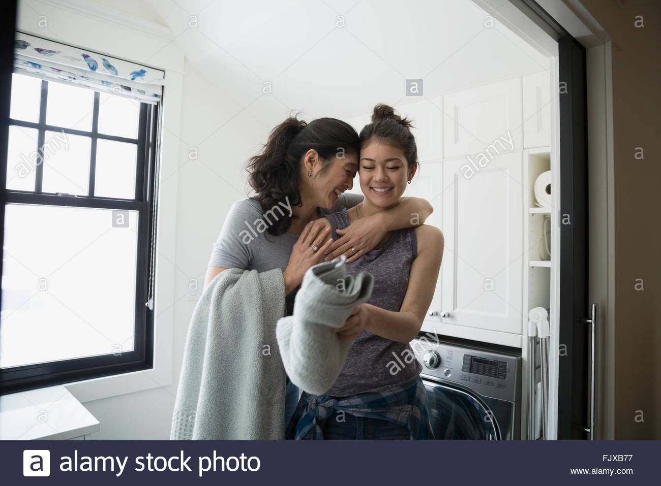 Mother hugging teenage daughter folding laundry Stock Photo