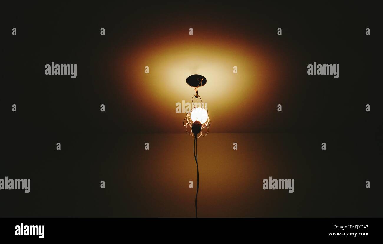 Low Angle View Of Illuminated Light Bulb Hanging From Ceiling Stock
