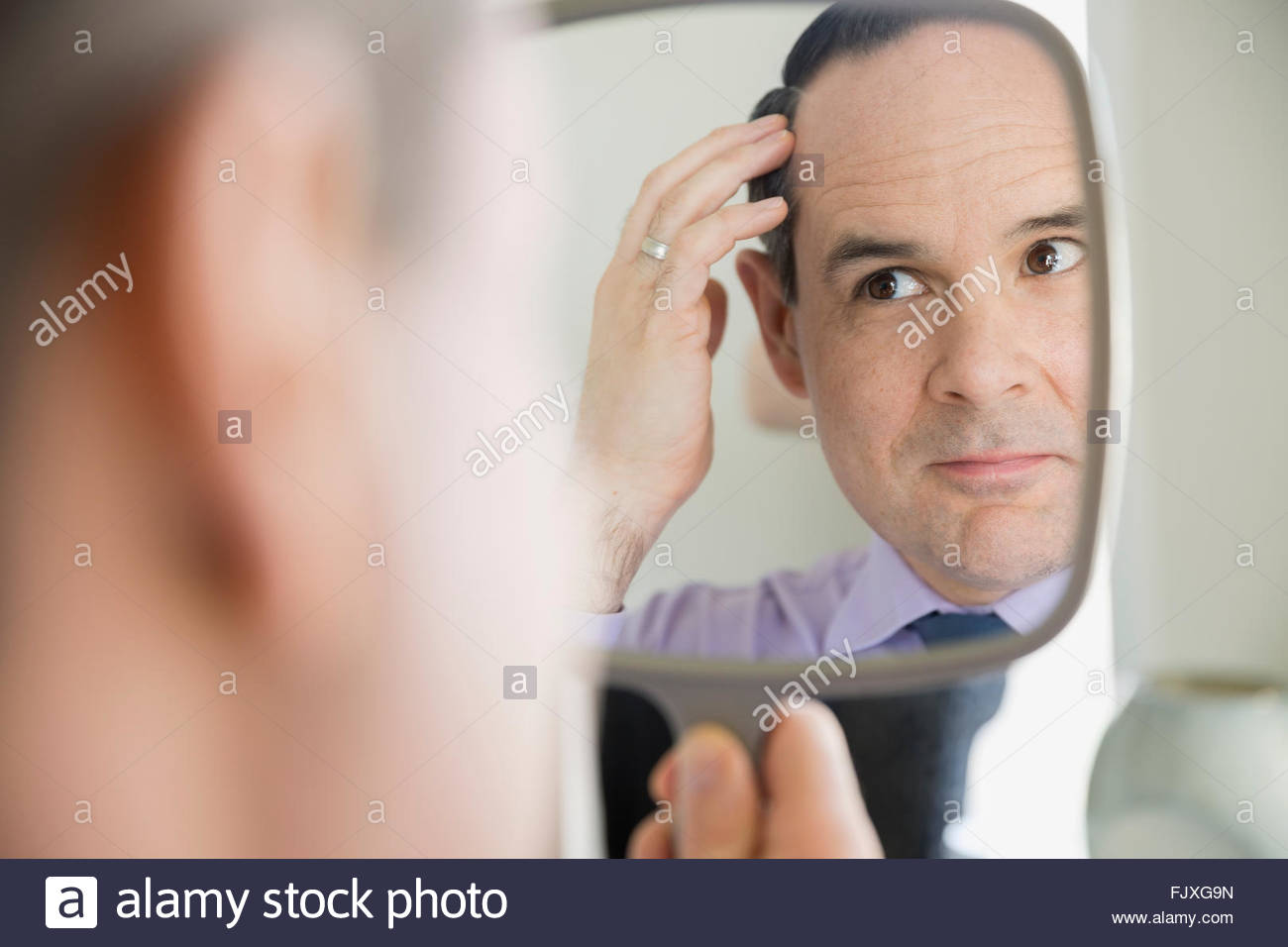 Man checking hair in hand mirror Stock Photo