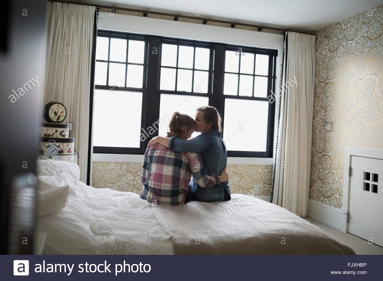 Mother hugging and kissing teenage daughter in bedroom Stock Photo