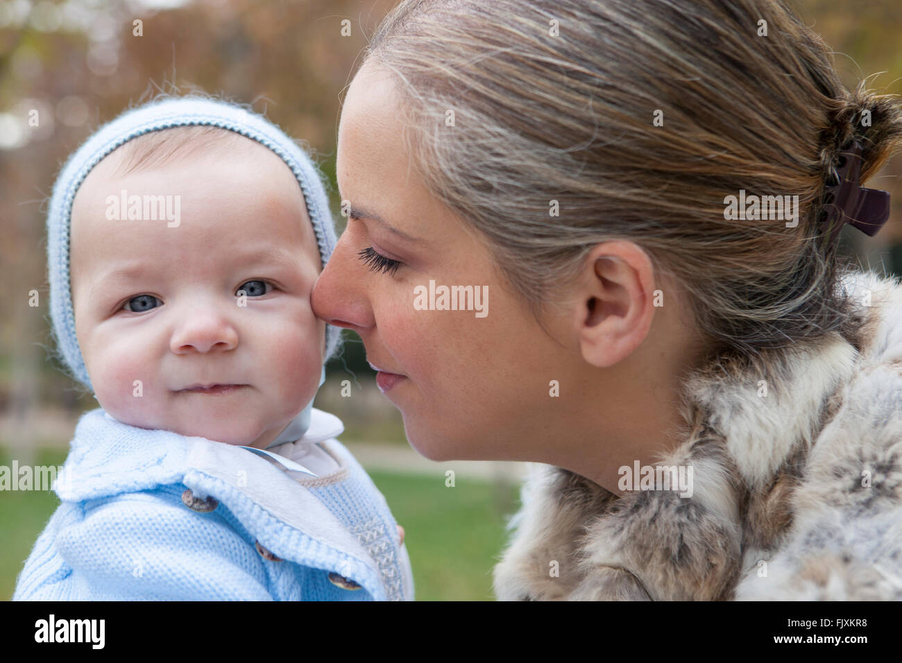 Happy mother playing with his baby in the park on the bench on winter season Stock Photo