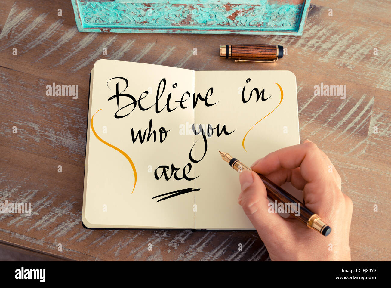 Retro effect and toned image of a woman hand writing a note with a fountain pen on a notebook. Handwritten text Believe in Who You Are as business concept image Stock Photo