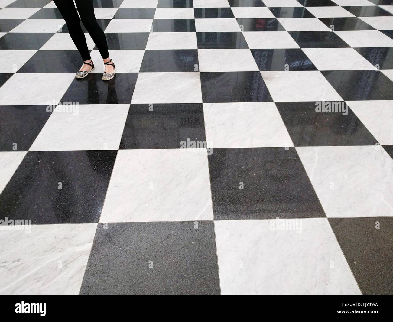 Low Section Of Woman Standing On Checked Pattern Floor Stock Photo