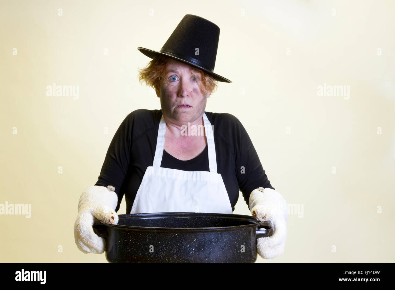 Mature woman with singed face holding roasting pan with pilgrim hat and apron. Stock Photo