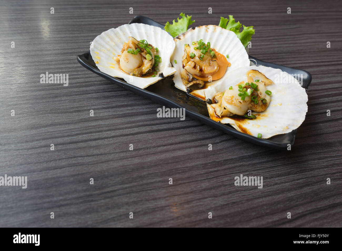 Three raw scallops on teriyaki sauce, copy space on the table Stock Photo