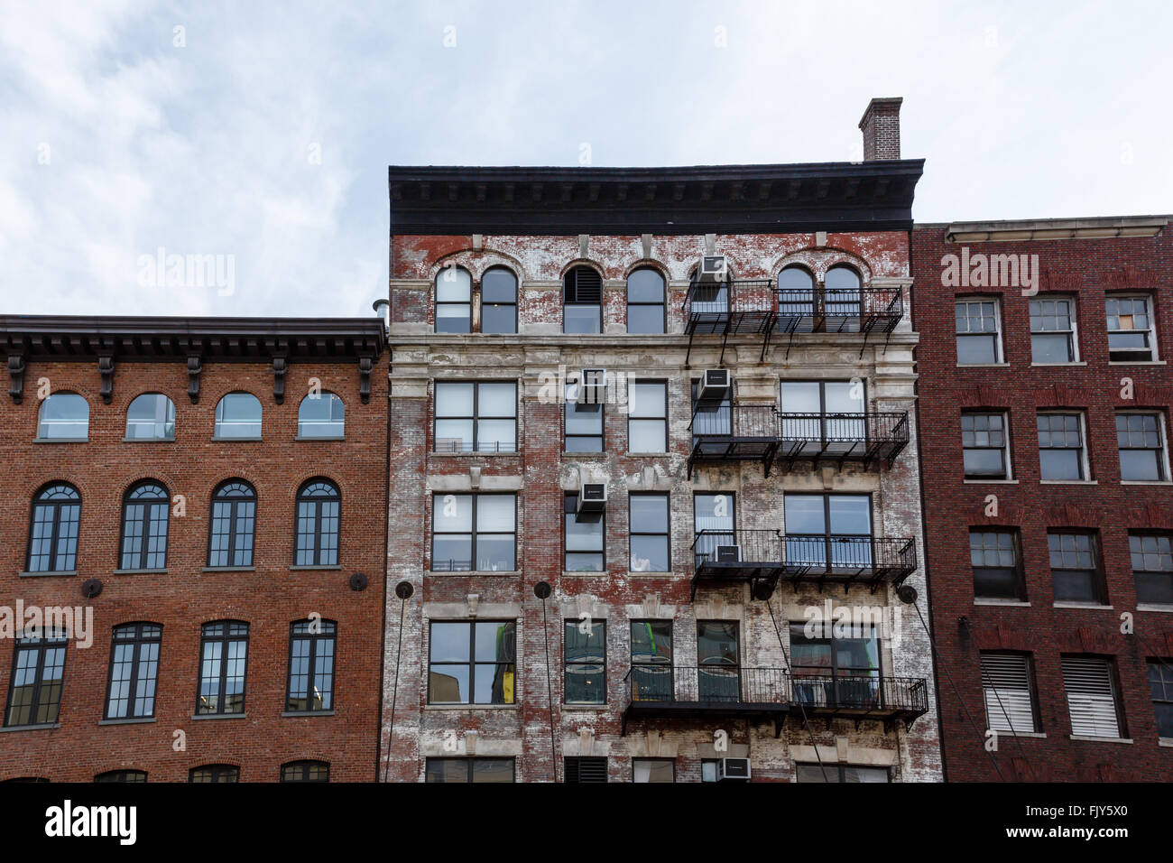 Pattern of fire escapes and window air conditioning units  on side of older brick building in New York City with blue sky above Stock Photo