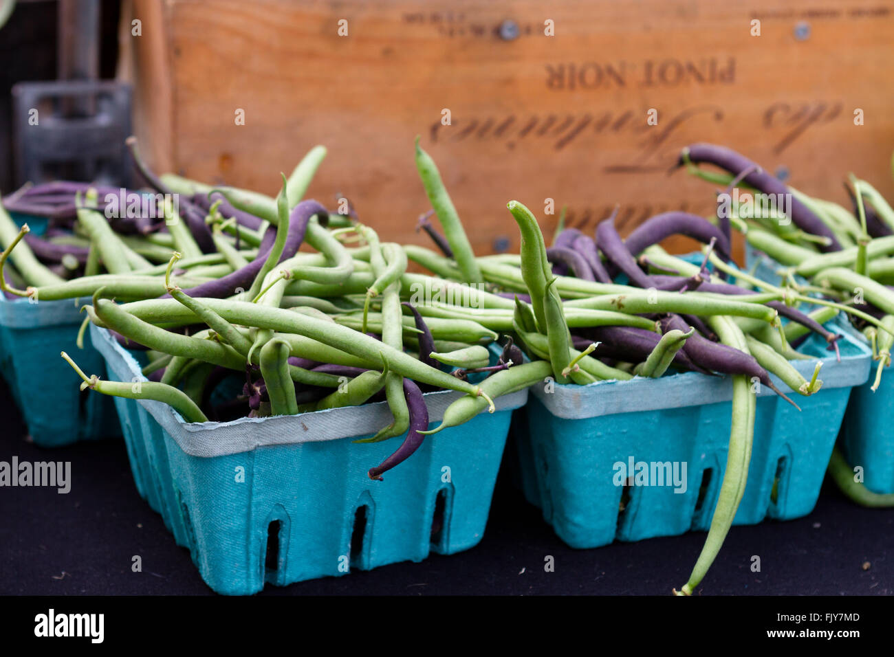 Green and purple beans in baskets with a rustic crate background at market Stock Photo