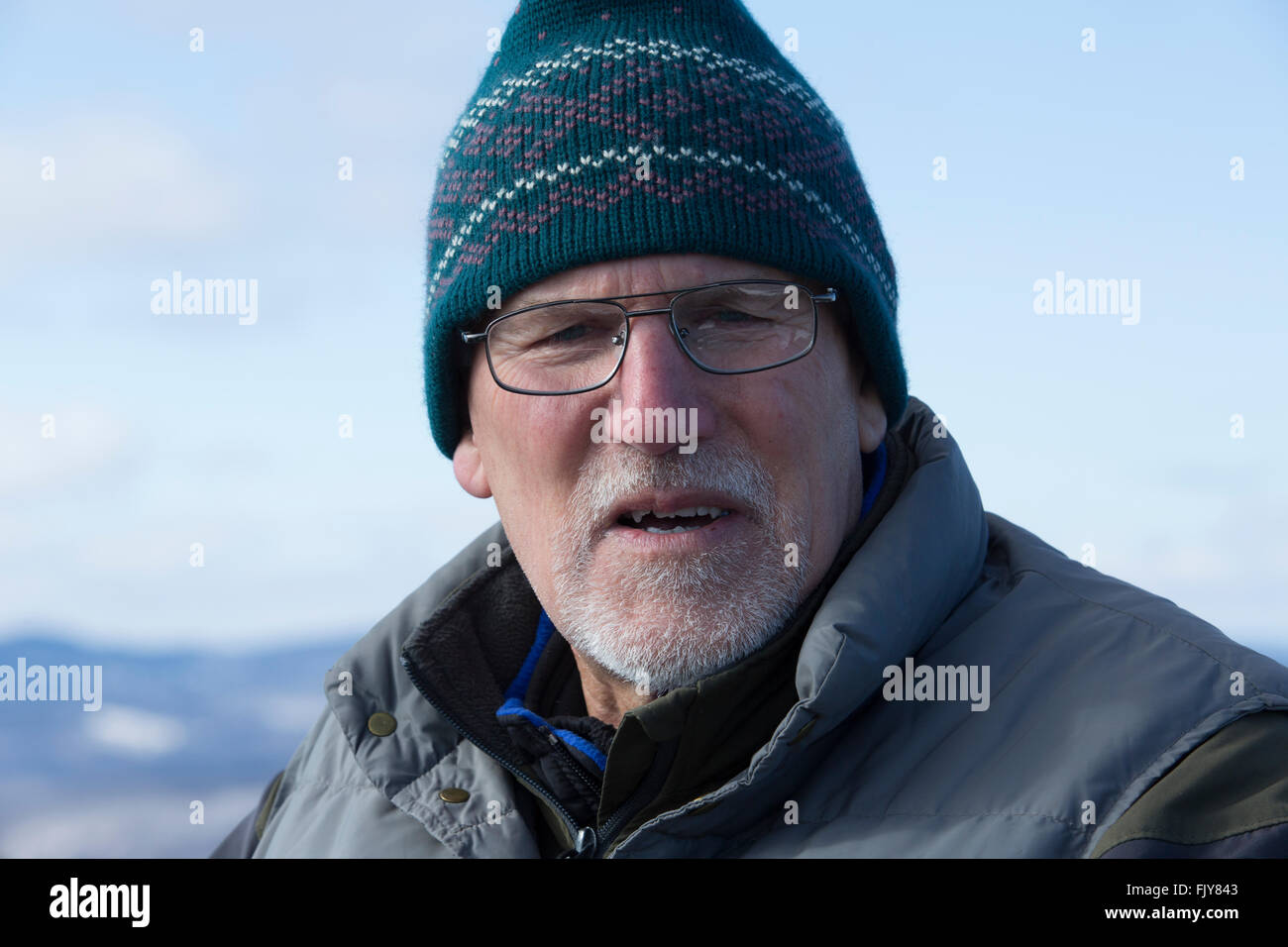 Senior man in cap and glasses on summit of Bald Mountain in winter, Rangeley, Maine. Stock Photo