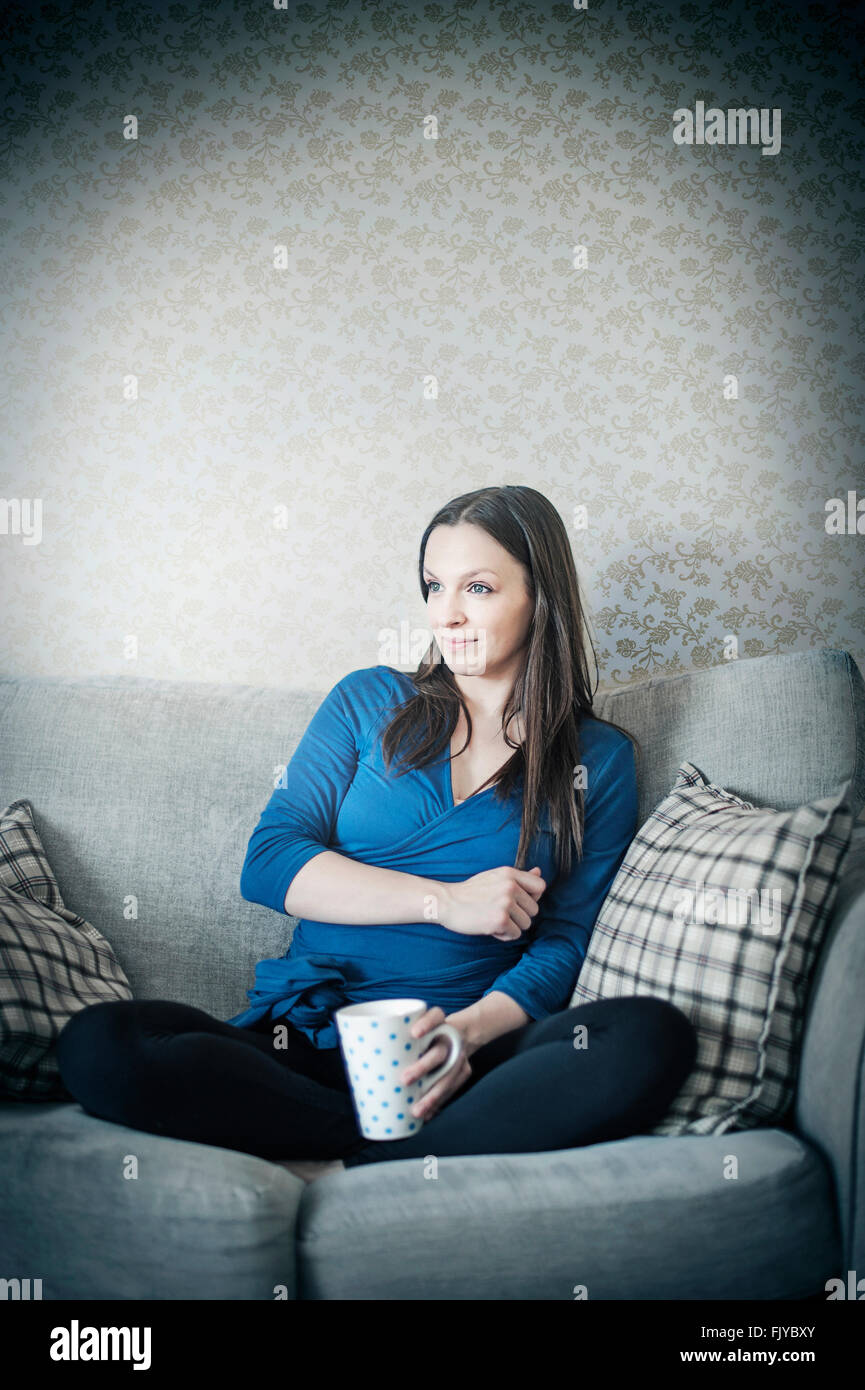 young woman resting on sofa bed with cup of tea Stock Photo