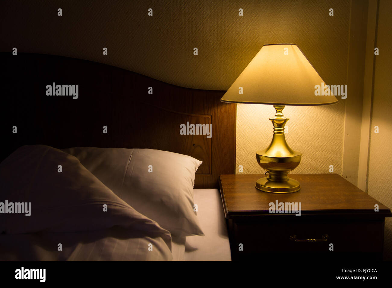 Lamp on a night table next to a bed spreading dimmed yellow light in the room Stock Photo