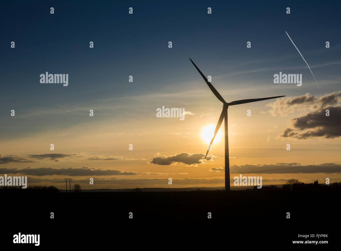 Wind turbine generator against sunset with airplane con trail overhead. Stock Photo