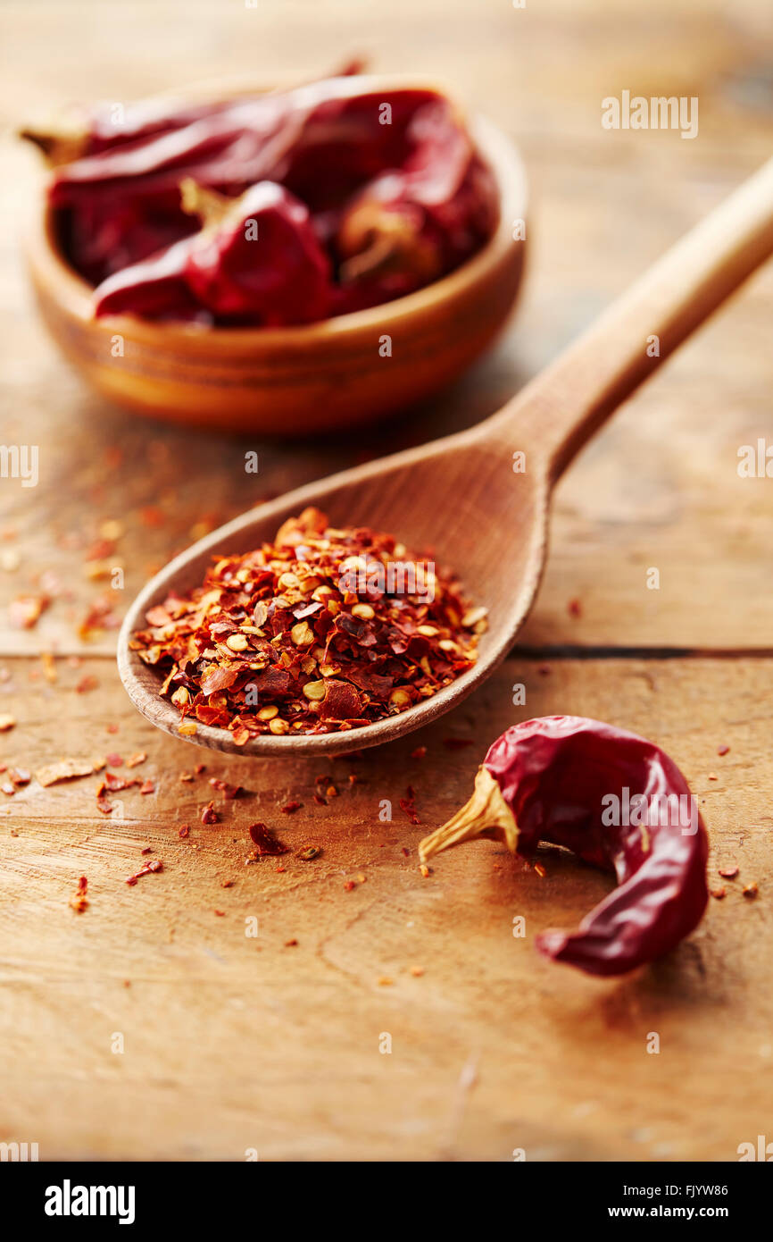 Wooden spoon with red chili pepper flakes and whole red peppers Stock Photo