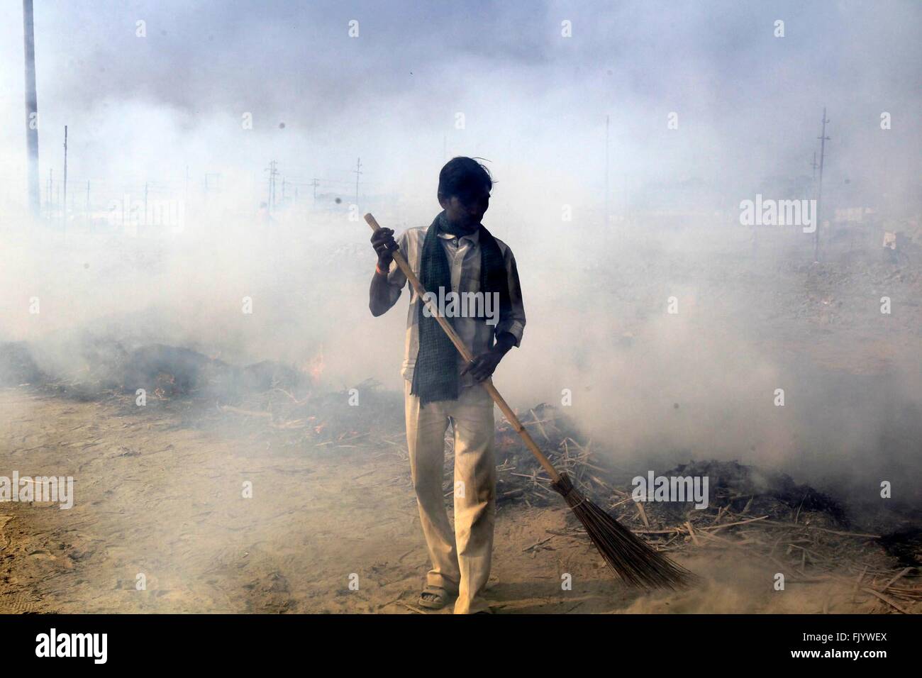 Allahabad, India. 03rd Mar, 2016. A man sweep near the smokes of burning garbage at the bank of the Ganga river after completion of the Magh Mela Festival in Allahabad. © Ravi Prakash/Pacific Press/Alamy Live News Stock Photo