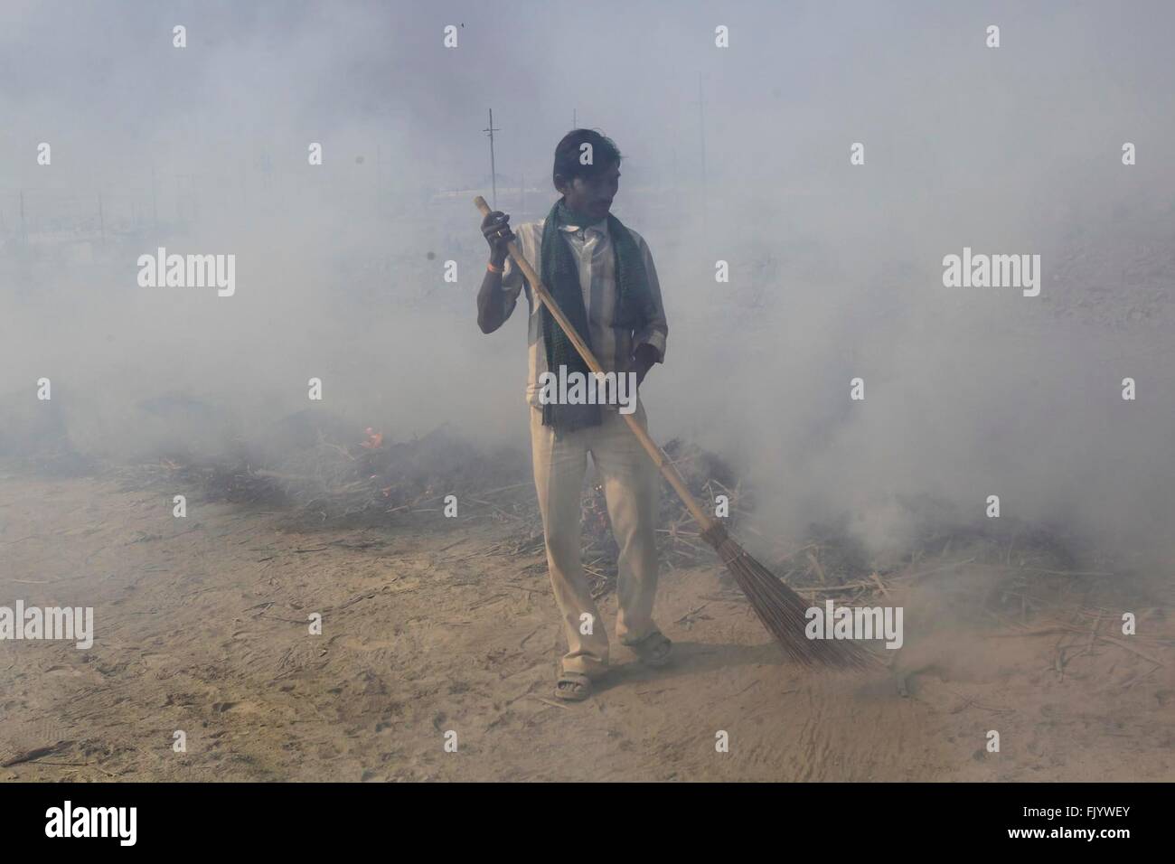 Allahabad, India. 03rd Mar, 2016. A man sweep near the smokes of burning garbage at the bank of the Ganga river after completion of the Magh Mela Festival in Allahabad. © Ravi Prakash/Pacific Press/Alamy Live News Stock Photo