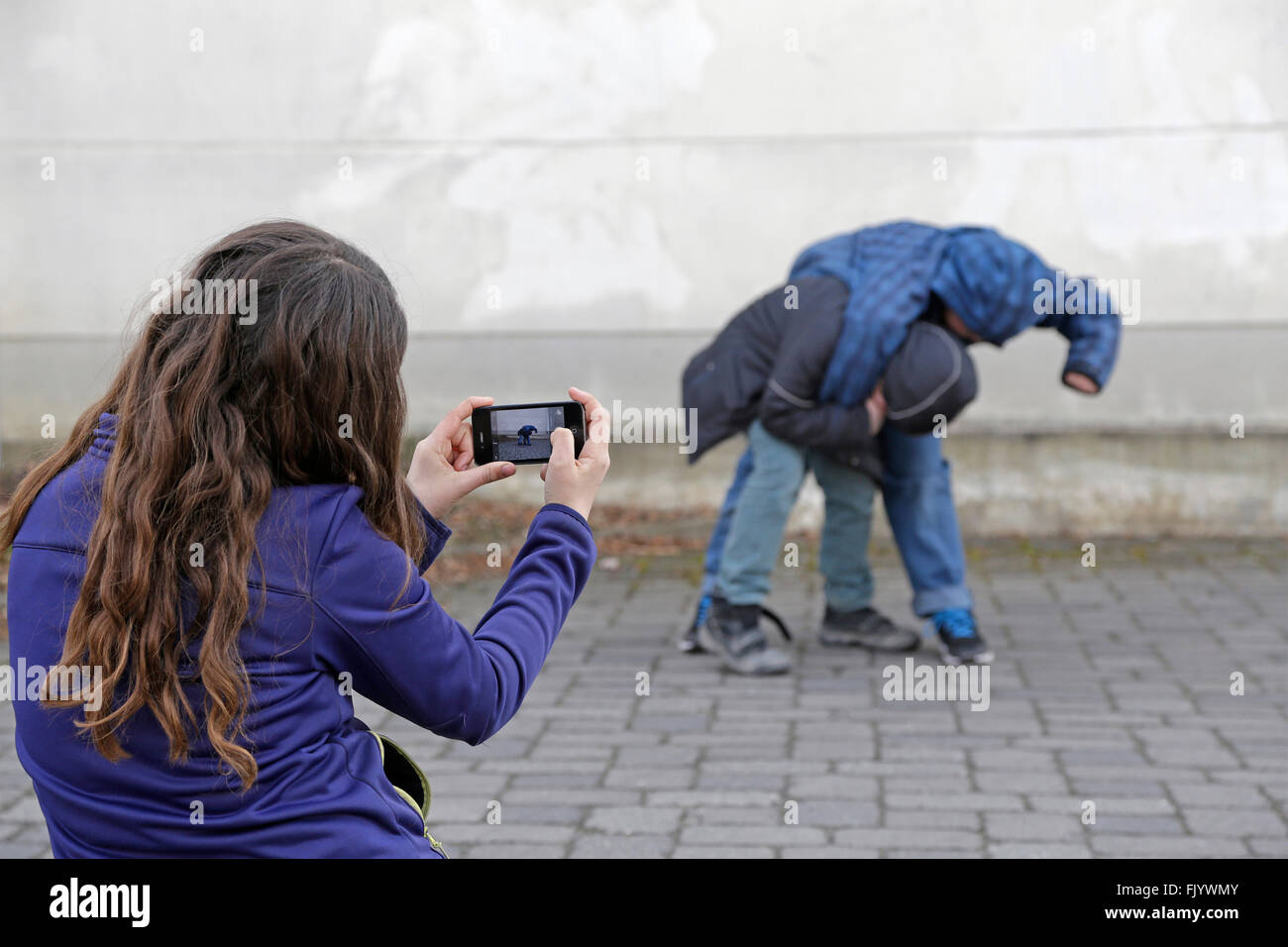 two kids fighting, third one making video with smartphone Stock Photo