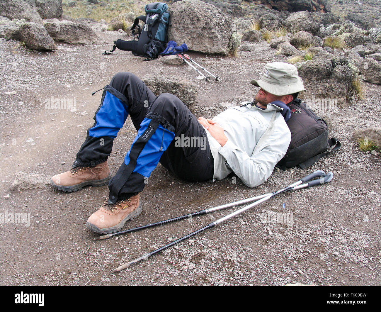 A man resting on the ground during a rest break while climbing Mount Kilimanjaro. Stock Photo