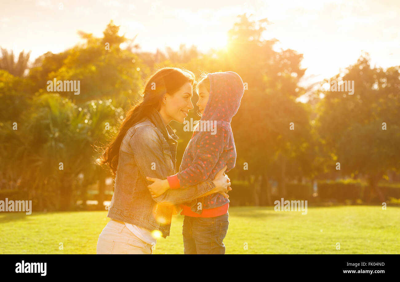 Side view on cheerful mother and daughter looking on each other, playing in the park in spring sunny day, happy family life Stock Photo