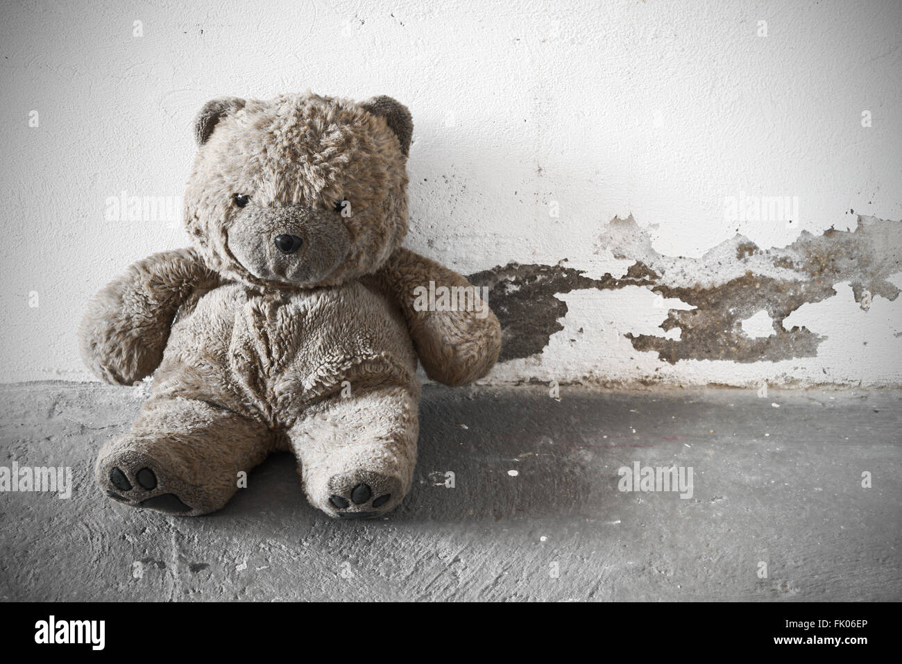 A old and dirty Teddy bear is sitting against a white concrete wall. vintage processing Stock Photo