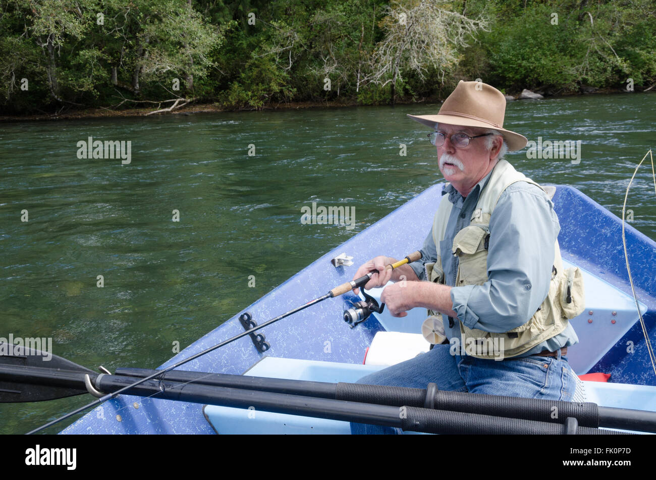 An elderly fisherman concentrates on catching the first trout of the day from his boat on the McKenzie River near Eugene, Oregon Stock Photo