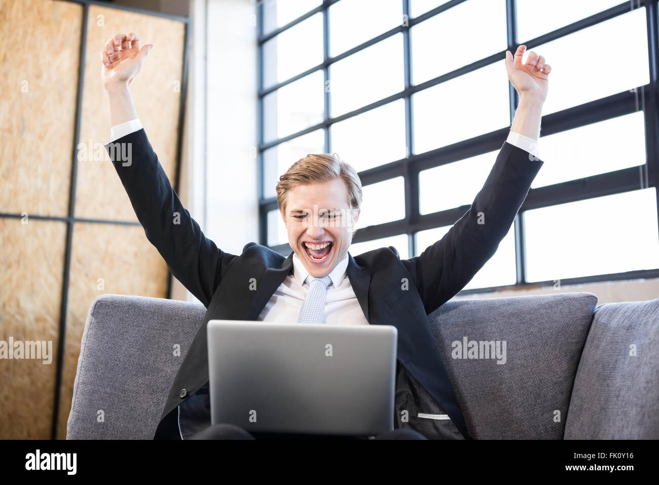 Businessman raising hands with excitement in front of laptop Stock Photo