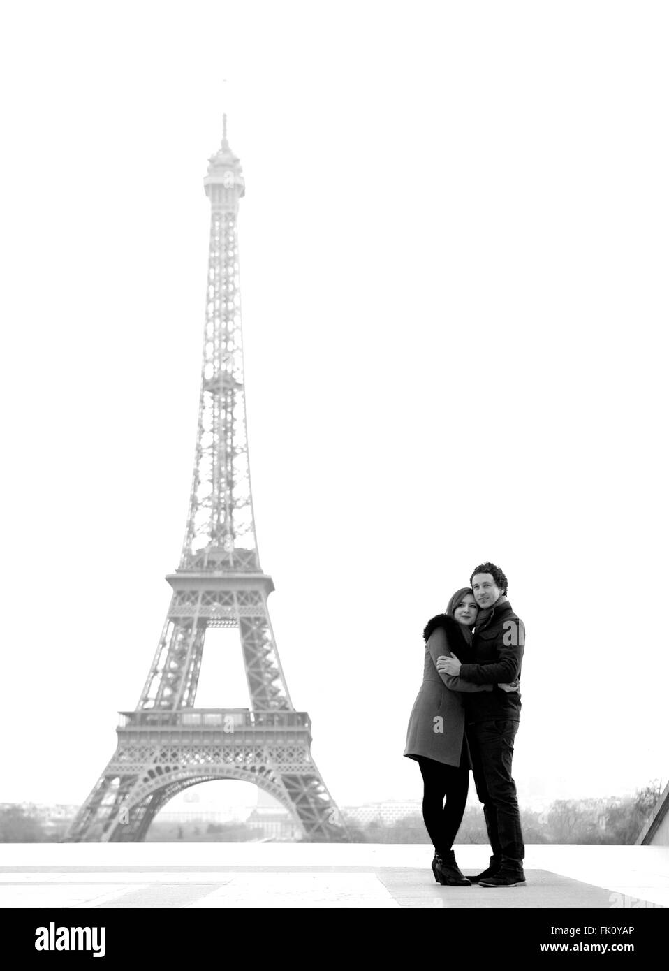 Young and in love brunette couple in front of Eiffel tower, Paris, at Trocadero overlooking the city during the day - hugging Stock Photo