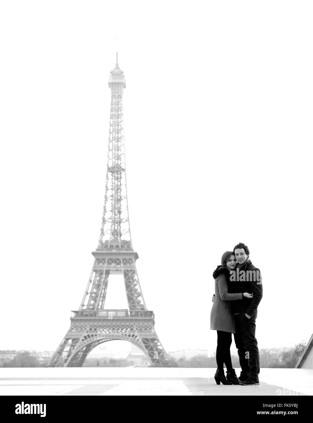 Young and in love brunette couple in front of Eiffel tower, Paris, at Trocadero overlooking the city during the day - hugging Stock Photo