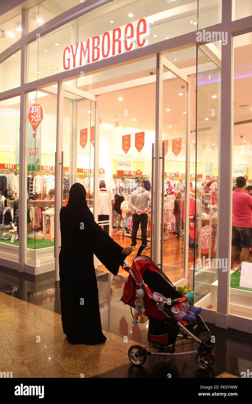 A muslim lady waits with her sleeping child outside shop in one of Dubai's major shopping malls while her husbond is shopping Stock Photo