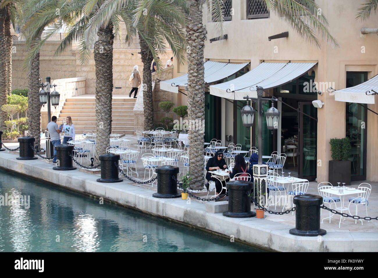 Blond chats with arab man, while arab ladies dine in Madinat Jumairah in quiet February afternoon. Stock Photo
