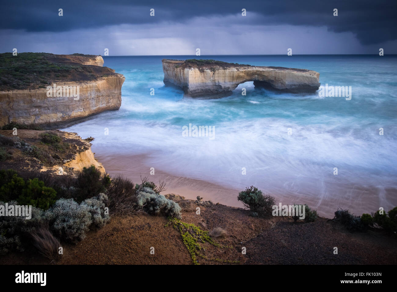 Rain showers pass the scenic natural arch formation, London Bridge (Arch), near Port Campbell along Victoria's Great Ocean Road. The arch was once connected to the mainland by a rock bridge, which unexpectedly collapsed on 15th January 1990, leaving two people stranded on the outer stack, who were later rescued by helicopter. Stock Photo
