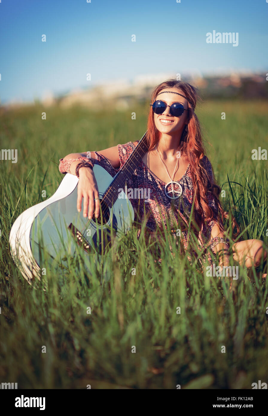 Portrait of a beautiful smiling hippie woman with guitar in the field Stock Photo