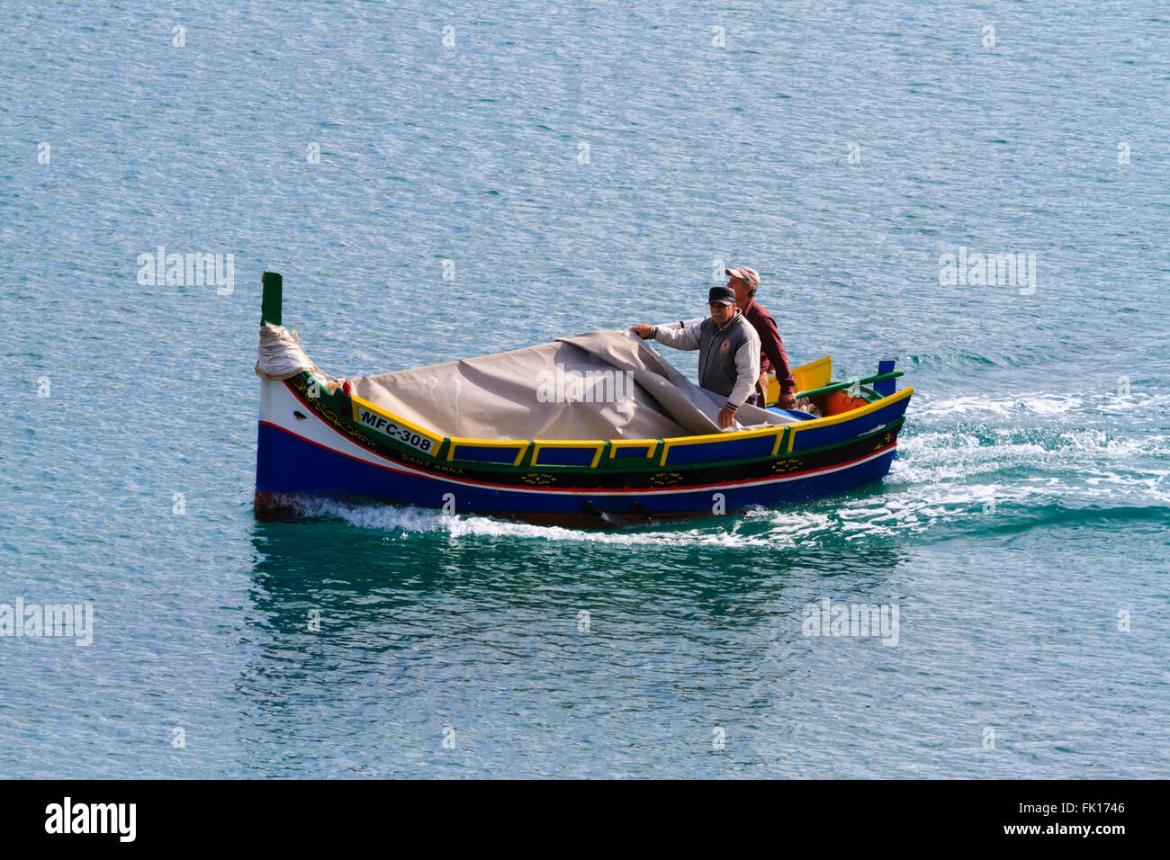 Traditional Maltese fishing boat with crew leaving Valletta, Grand harbour Stock Photo