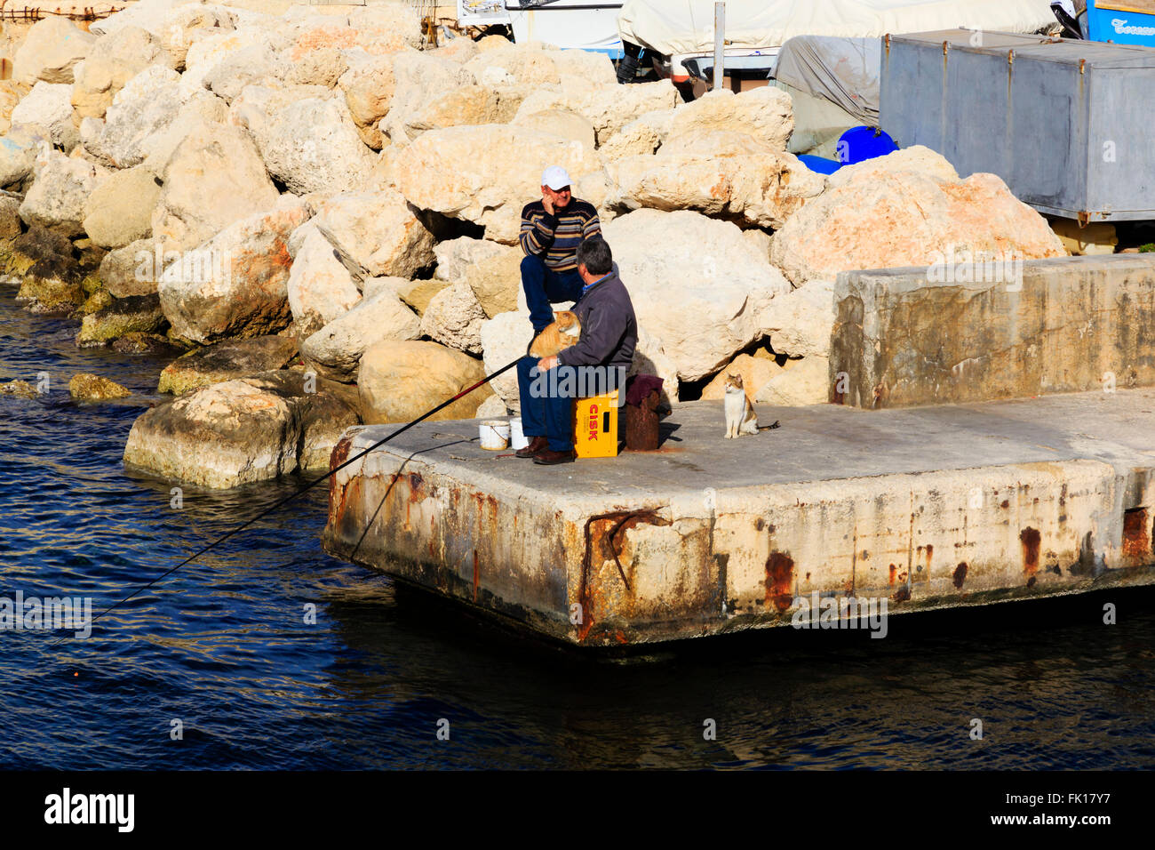Two Maltese men fishing with cats waiting patiently. Floriana, Valletta, Malta Stock Photo