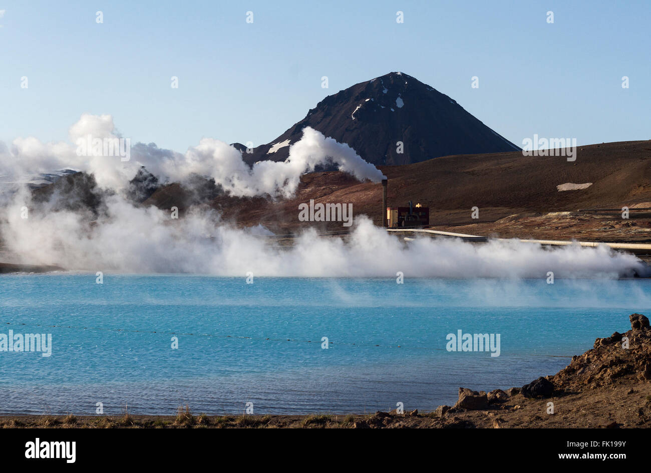 Horizontal view of an Icelandic geothermal power facility near a hot spring and tall mountains in the background Stock Photo
