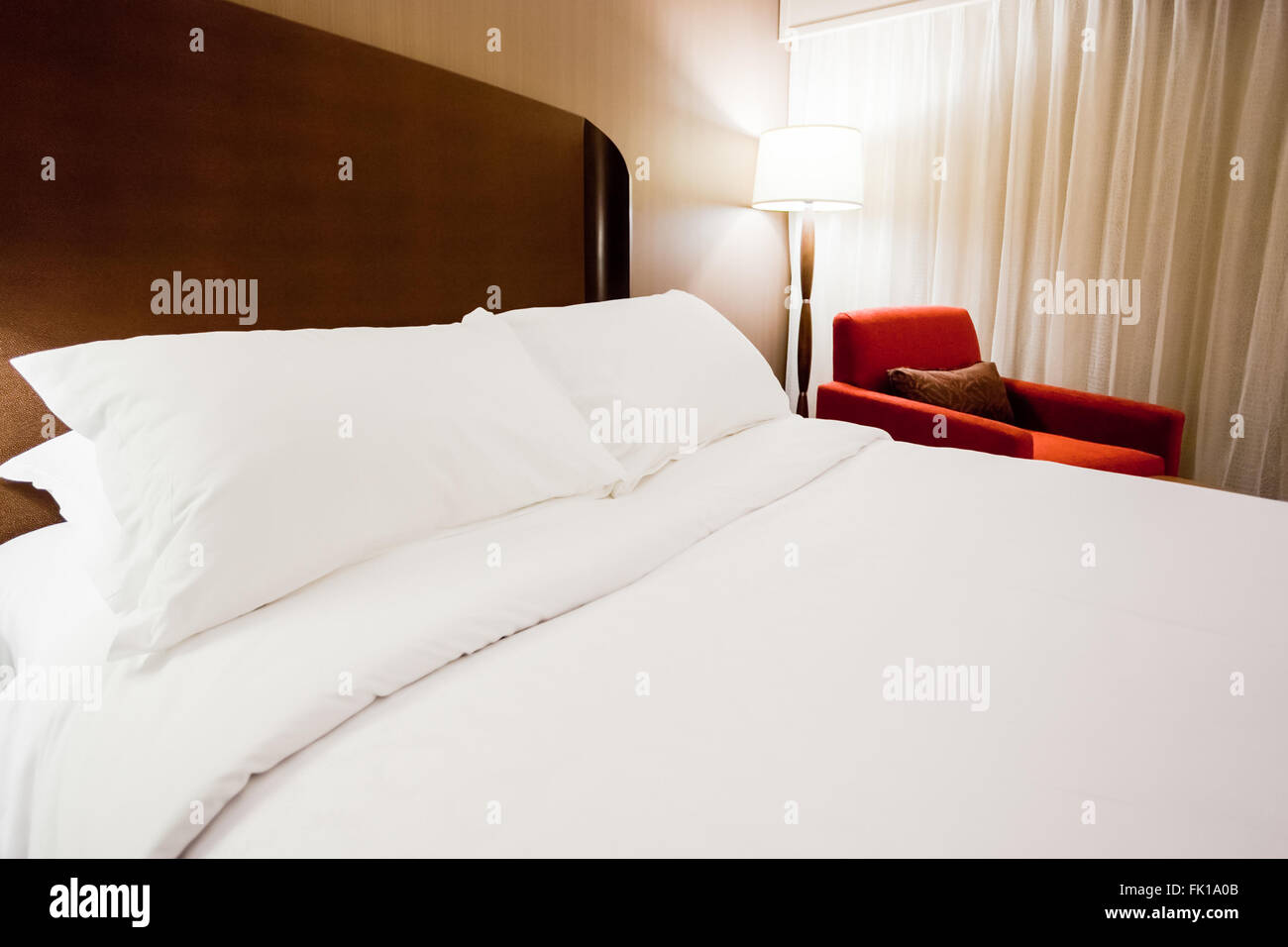 Modern hotel room with a bed, lamp and red chair Stock Photo