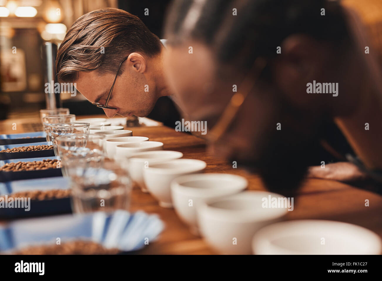 Baristas bending over rows of fresh coffee at a tasting Stock Photo
